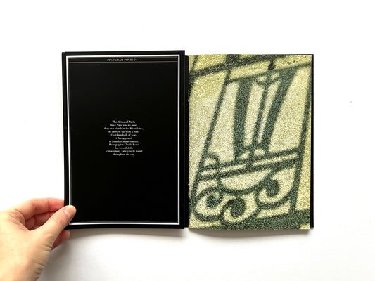 Open spread of Pentagram Papers 24 “The Arms of Paris”, showing a black title page with centered text on the left and a full-page grainy green-toned photographic image on the right, with a hand holding the booklet against a white background.