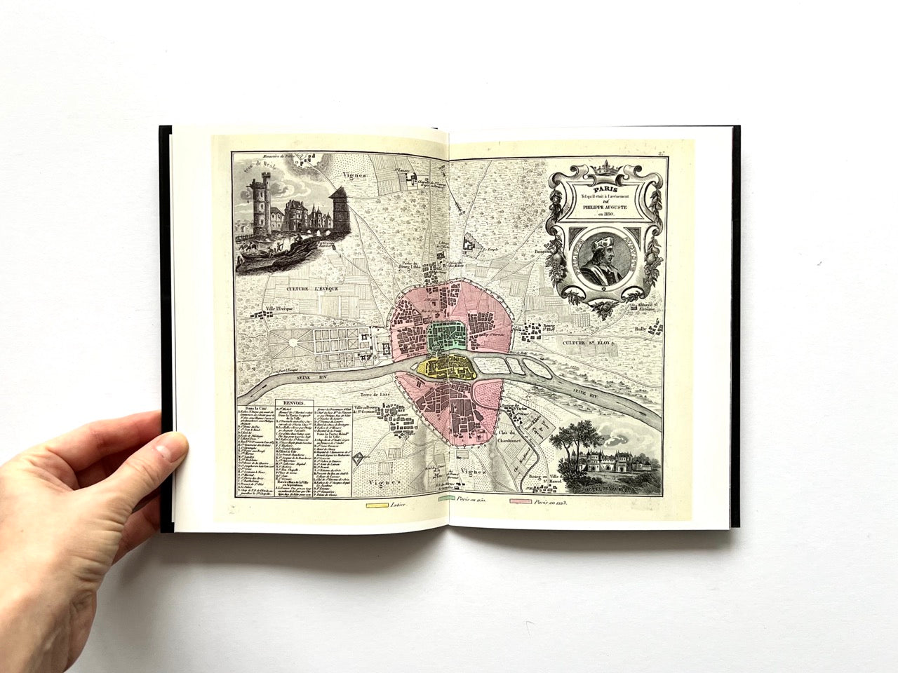 Open spread of Pentagram Papers 24 “The Arms of Paris”, showing a historic illustrated map of Paris with colour-coded districts and decorative cartouches, held open by a hand against a white background.