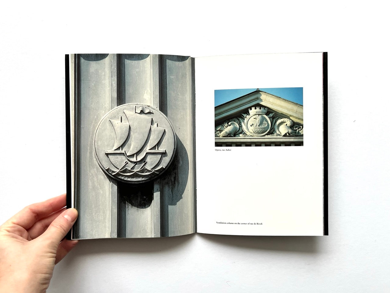 Open spread of Pentagram Papers 24 “The Arms of Paris”, showing a full-page photograph of a circular stone relief with sailing ships on the left and two smaller architectural photographs of Parisian building details on the right, held open by a hand against a white background.
