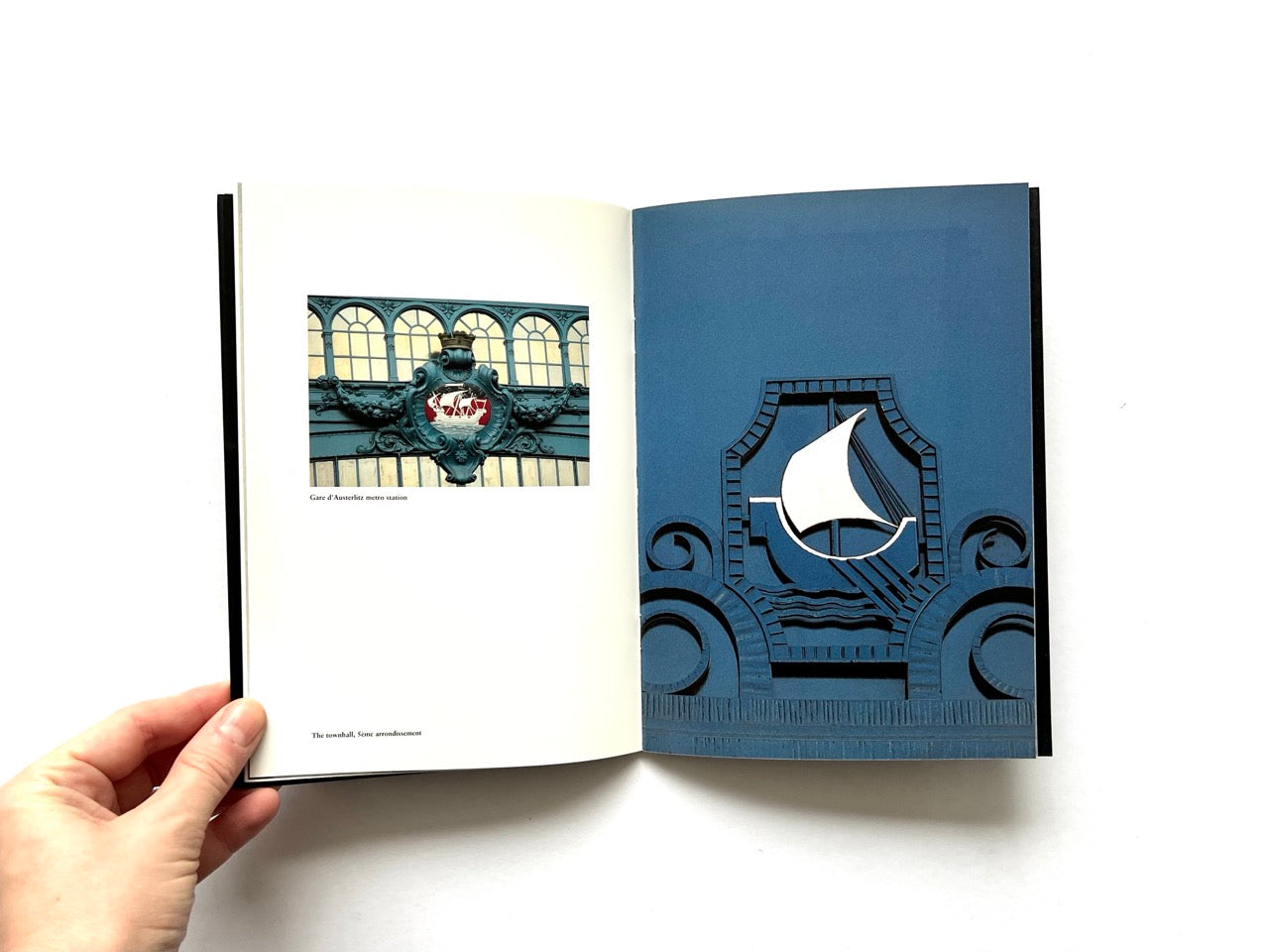 Open spread of Pentagram Papers 24 “The Arms of Paris”, showing a small photograph of an architectural crest with a ship motif on the left page and a full-page blue-toned relief emblem featuring a stylised sailing ship on the right, held open by a hand against a white background.