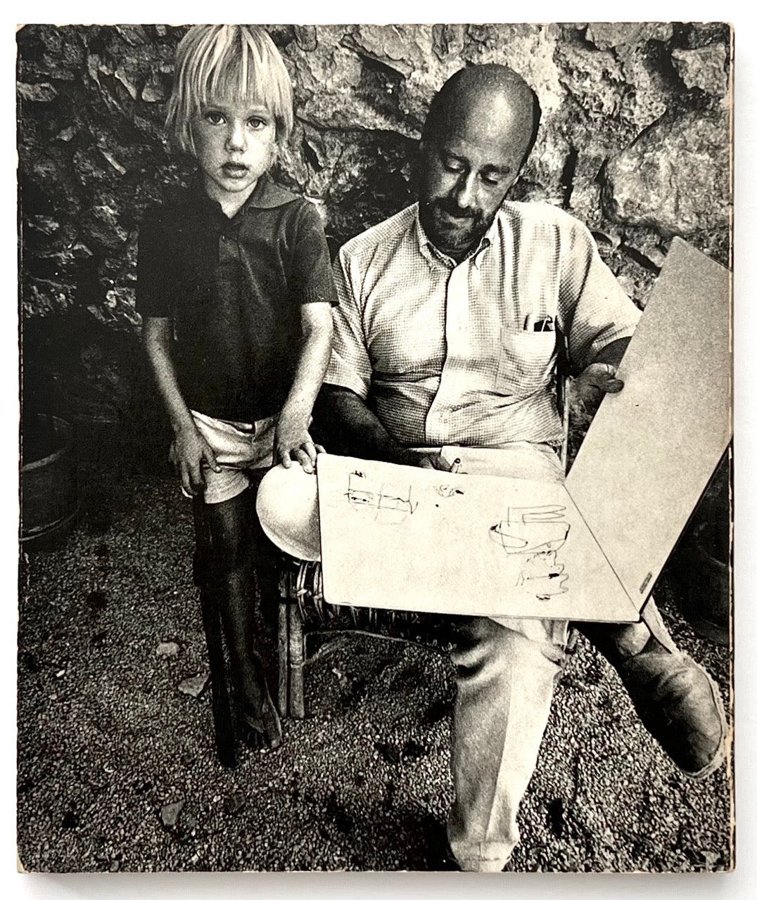 Back cover of The Artist as Reporter showing black and white photograph of Paul Hogarth sketching outdoors with a child standing beside him.