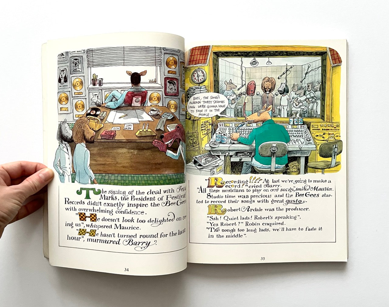 Open book - 'The Legend: The Illustrated Story of the Bee Gees' - with illustrated pages showing a scene inside a recording studio and an office.