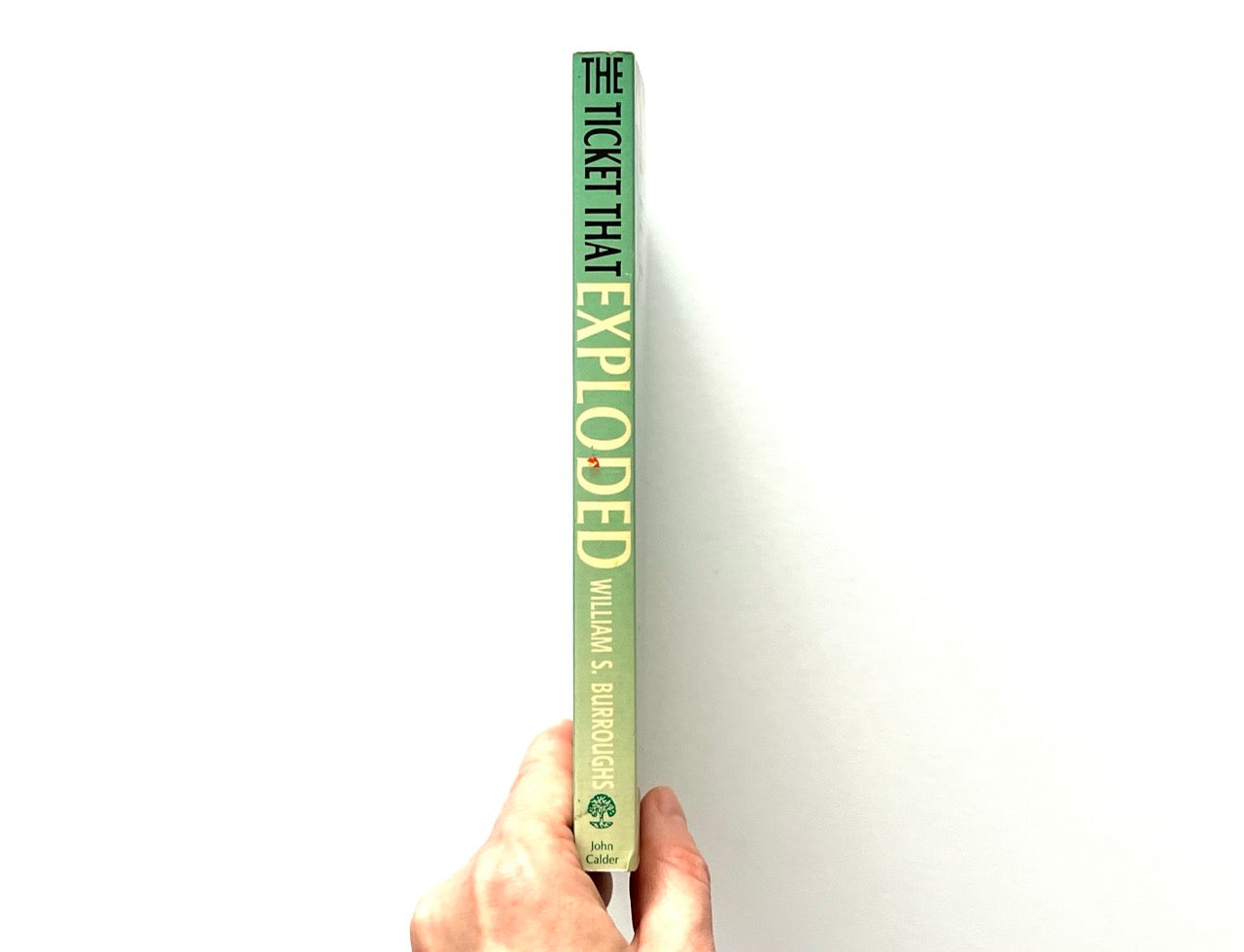 Book titled 'The Ticket That Exploded' held by a hand on a white background