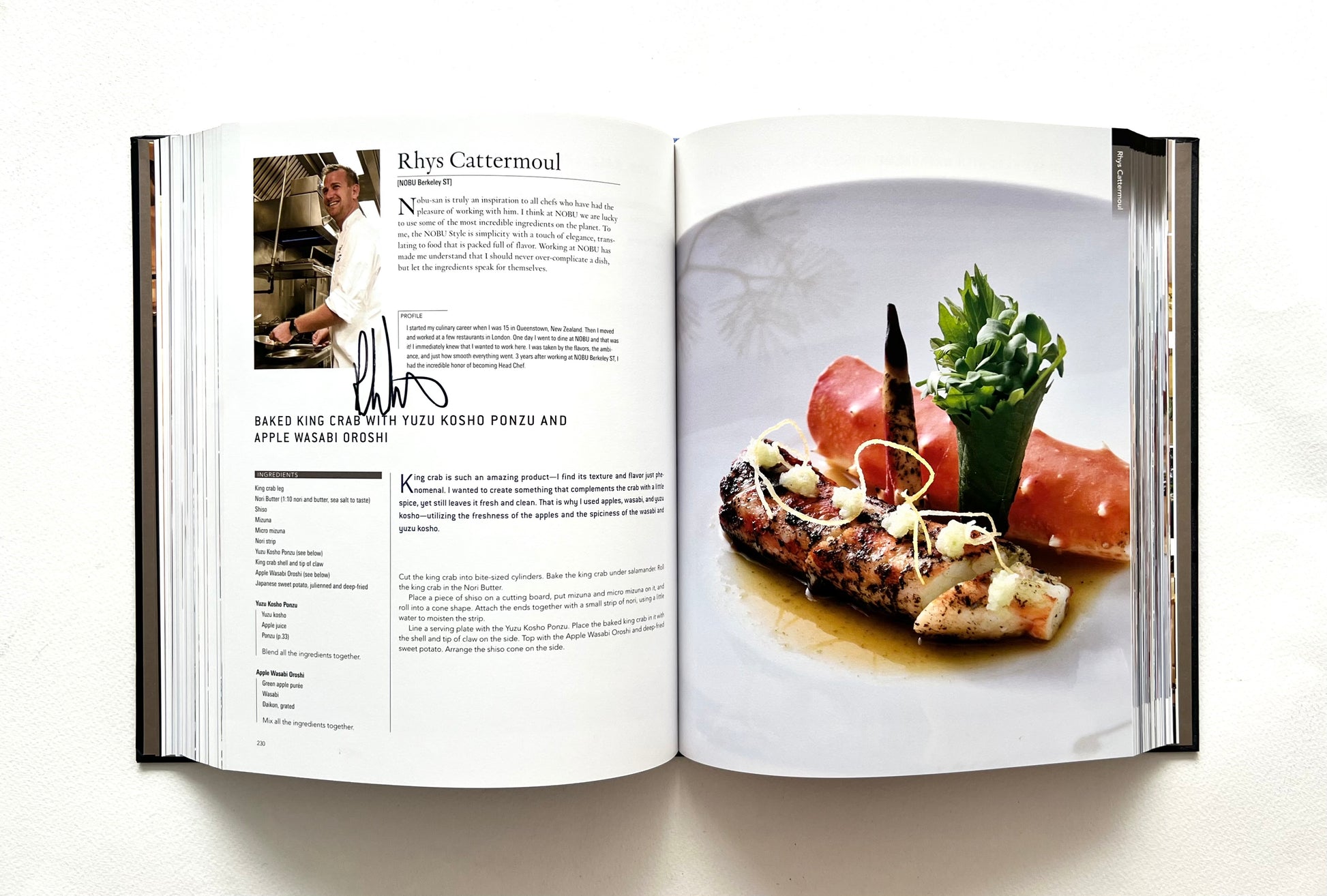 Open "World of Nobu" cookbook showing a recipe with a photograph of a BAKED KING CRAB WITH YUZU KOSHO PONZU AND APPLE WASABI OROSHI dish - signed by chef Rhys Cattermoul.