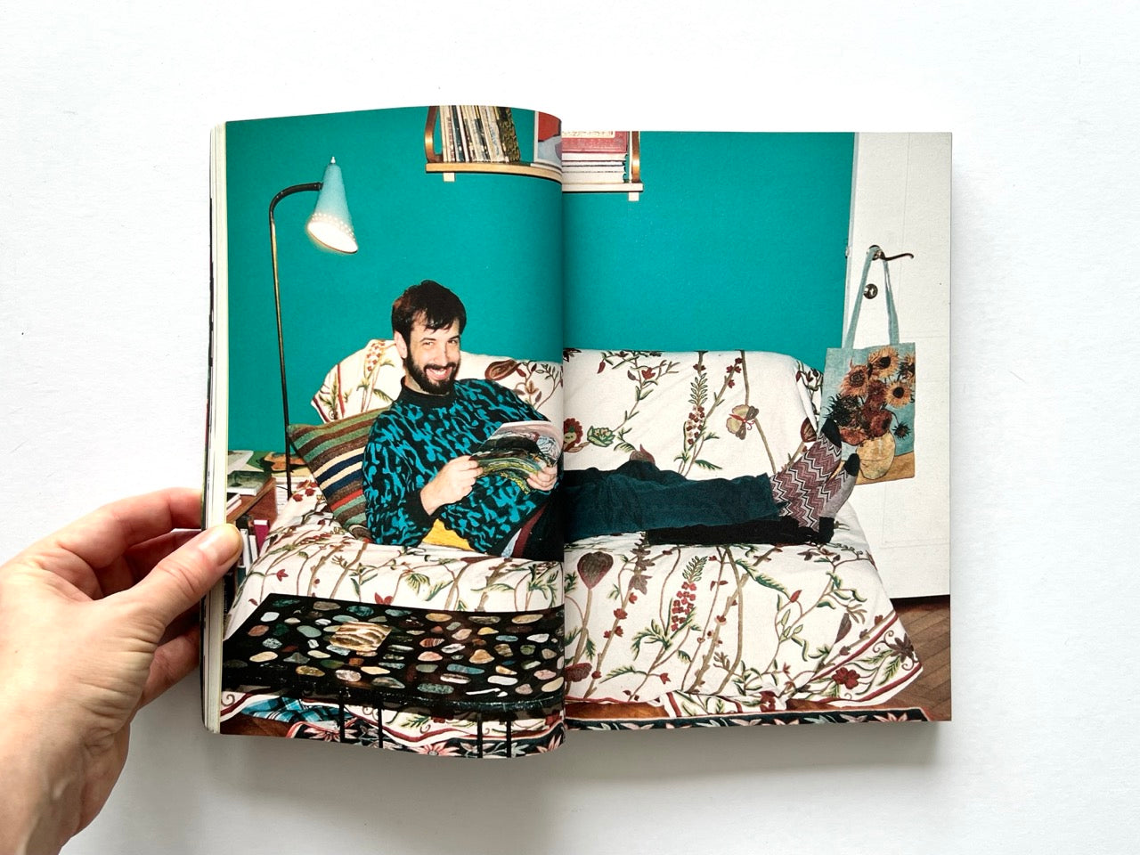 Apartamento Magazine Issue #21  – Interior spread showing a man reclining on a patterned sofa in a colourful living room, reading a magazine with eclectic decor.