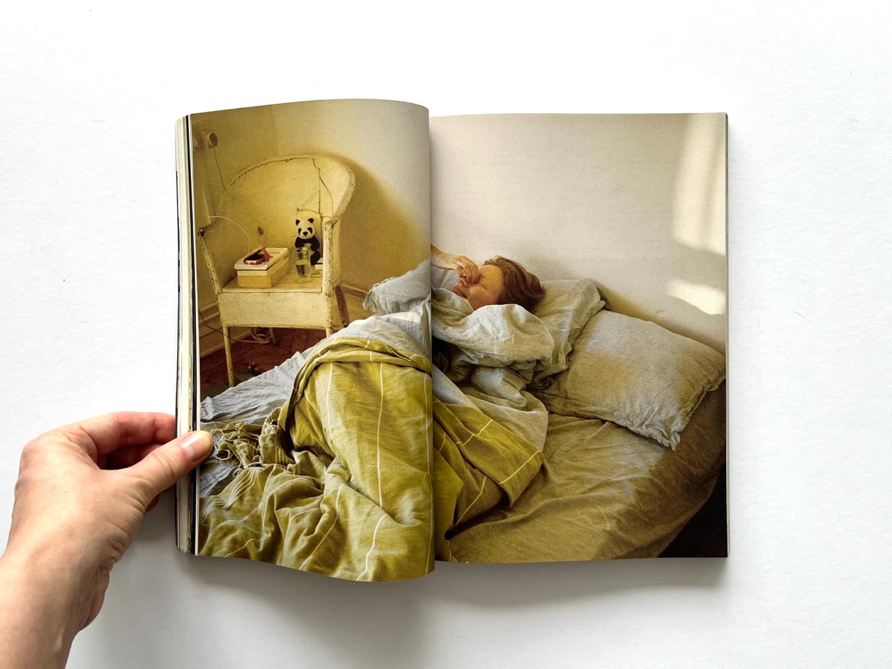 Apartamento Magazine Issue #21 – Interior spread showing a person lying in bed in soft morning light, with a bedside table, wicker chair, and minimal domestic setting.