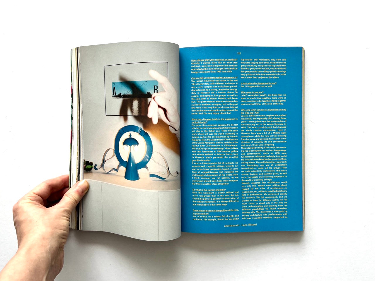 Apartamento Magazine Issue #21 – Interior spread featuring a design object display with a hand pointing at artwork, opposite a blue text-heavy editorial page.
