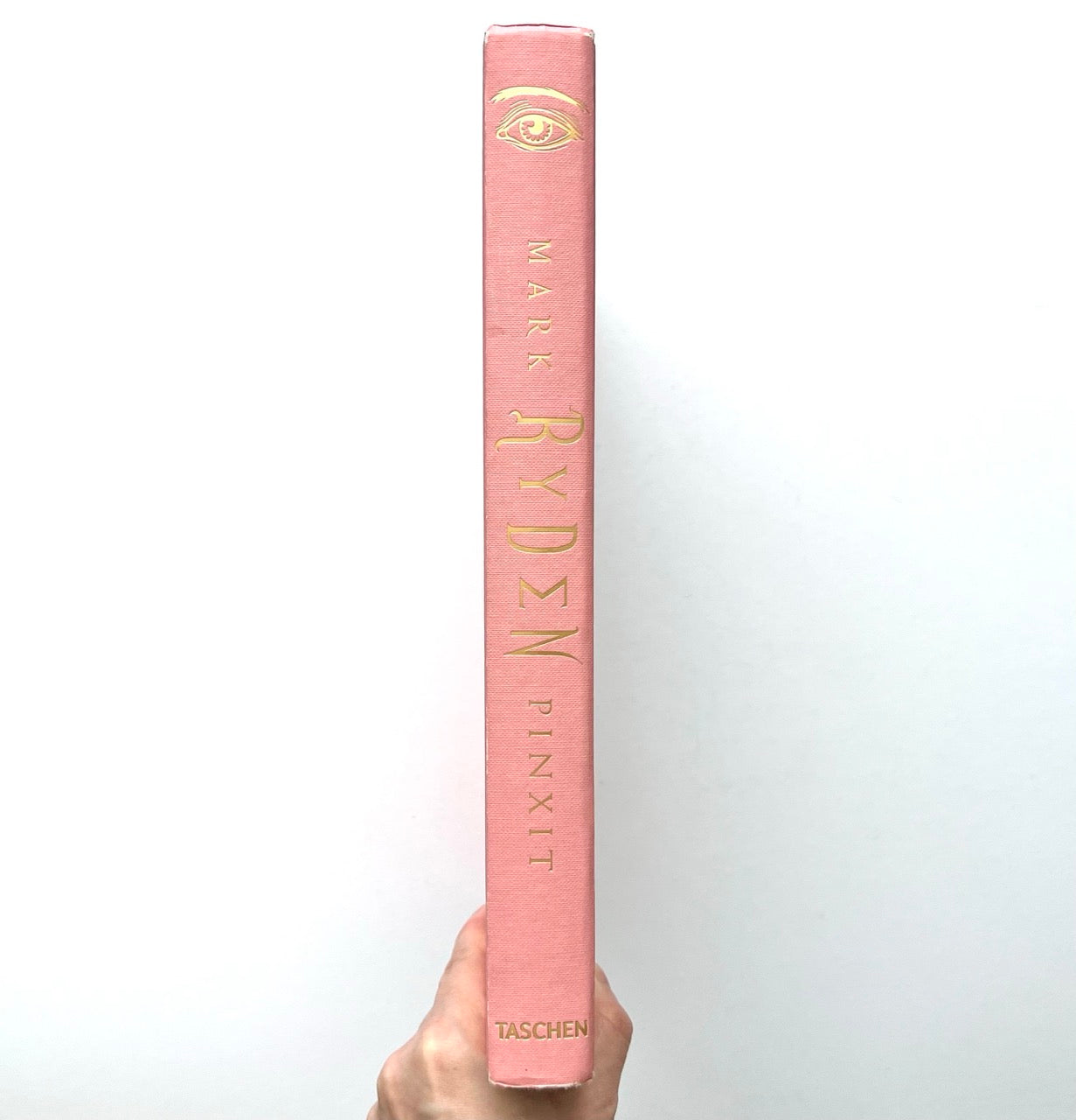 Mark Ryden Pinxit book spine showing pink cloth binding with gold lettering and eye motif