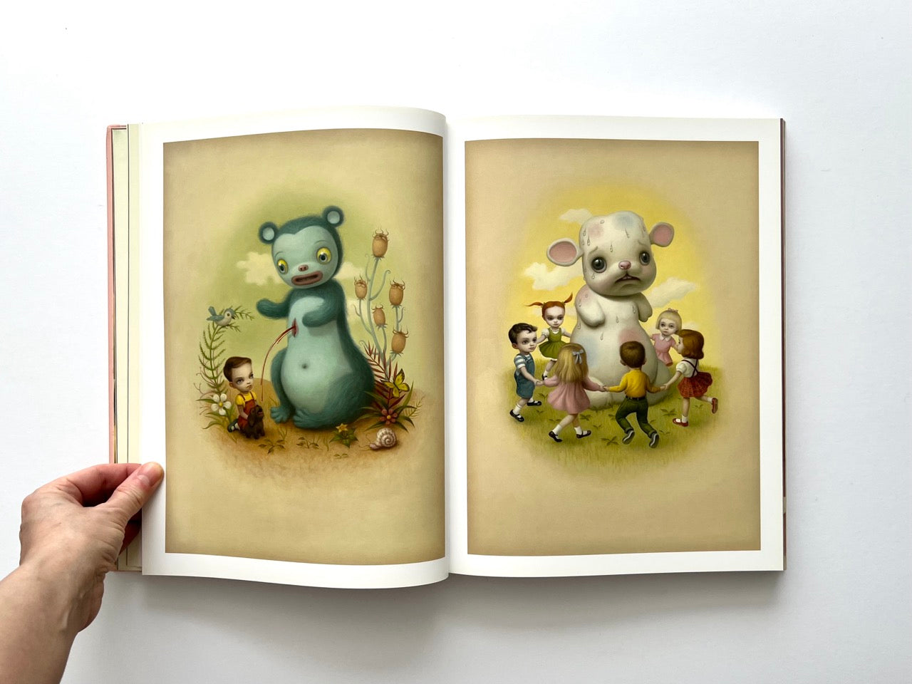Mark Ryden Pinxit interior spread showing two paintings of children with anthropomorphic animals including a blue bear figure and a large white creature surrounded by children