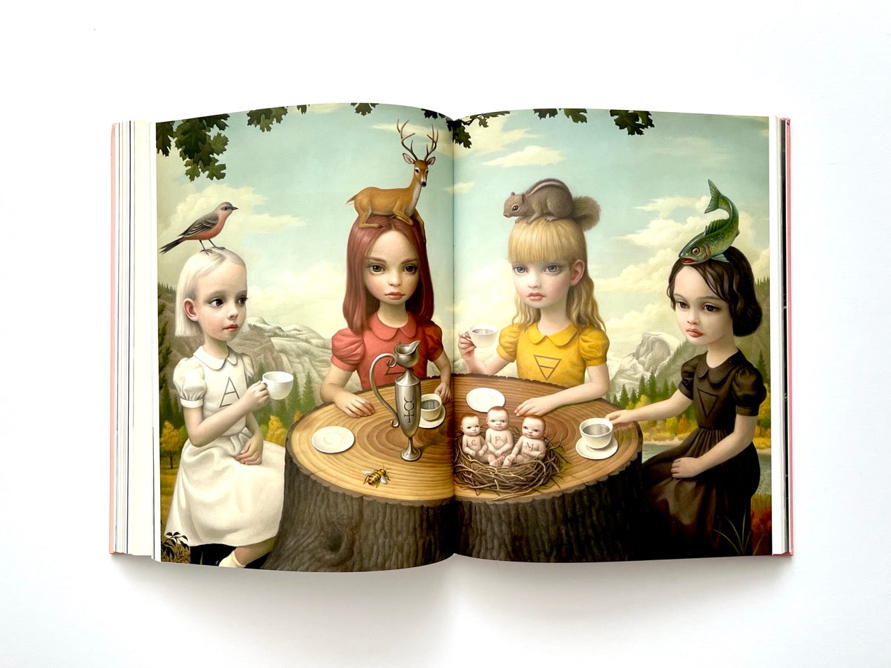 Mark Ryden Pinxit interior spread featuring four girls seated around a tree-stump table with teacups, animals perched on their heads, and symbolic figures in a surreal outdoor scene