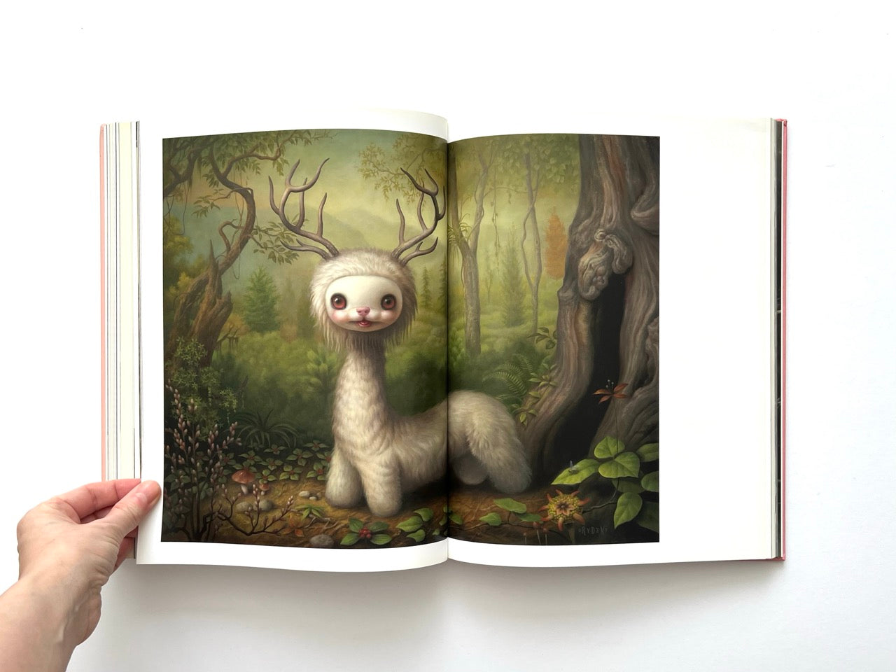 Mark Ryden Pinxit interior spread featuring a whimsical deer-like creature with antlers and a soft, elongated body standing in a lush forest clearing