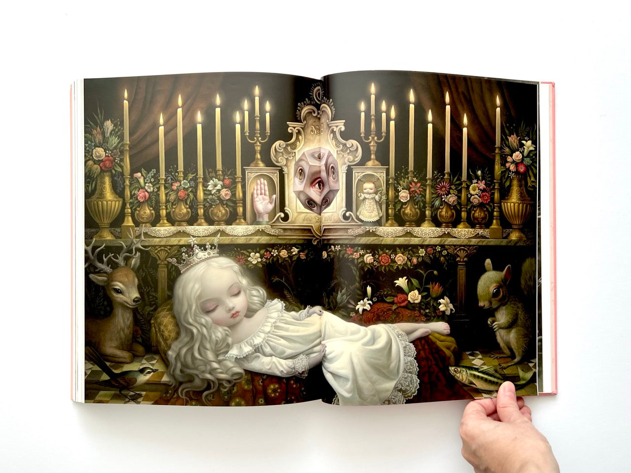 Mark Ryden Pinxit interior spread showing a sleeping girl in a white dress laid out beneath an ornate altar with candles, flowers, and symbolic objects in a dreamlike setting