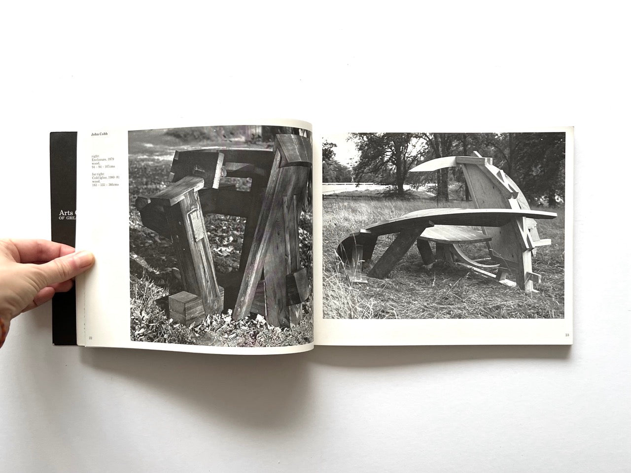 Open spread from “The Sculpture Show” (1983) showing two outdoor sculptures by John Cobb photographed in black and white, each constructed from stacked or interlocking timber forms set in a natural landscape.