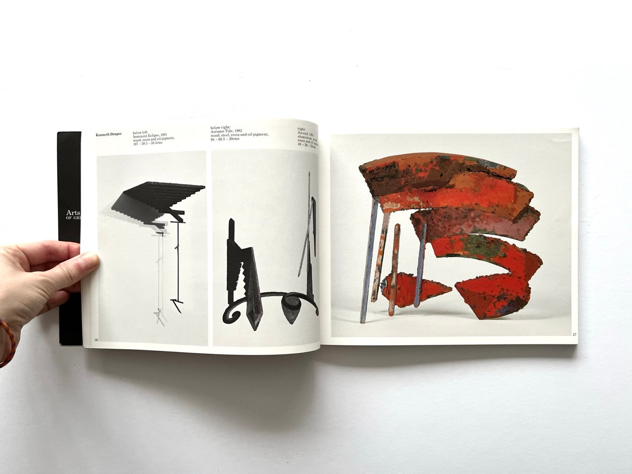 Open spread from “The Sculpture Show” (1983) featuring two black-and-white images of slender abstract metal sculptures on the left, and a colour photograph on the right of a multi-panel sculptural form made of curved red and orange painted elements.
