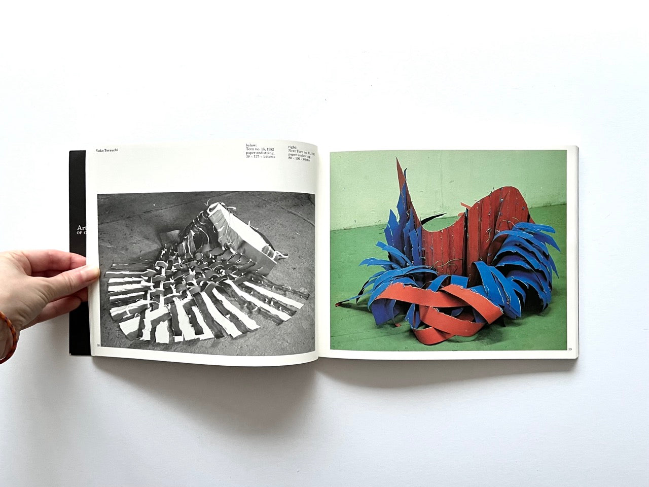 Open spread from “The Sculpture Show” (1983) featuring a black-and-white photograph of a woven, folded sculptural structure on the left, and a colour photograph on the right of a vibrant red and blue abstract installation made from curved metal or fabric strips.