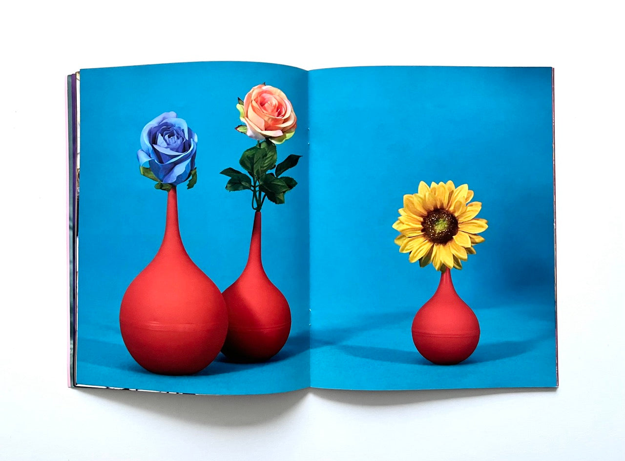 Magazine spread (Toiletpaper No. 7, December 2012) showing three red bolbous vases photographed against bright blue background, with hyper-coloured single flowers placed in each of them.
