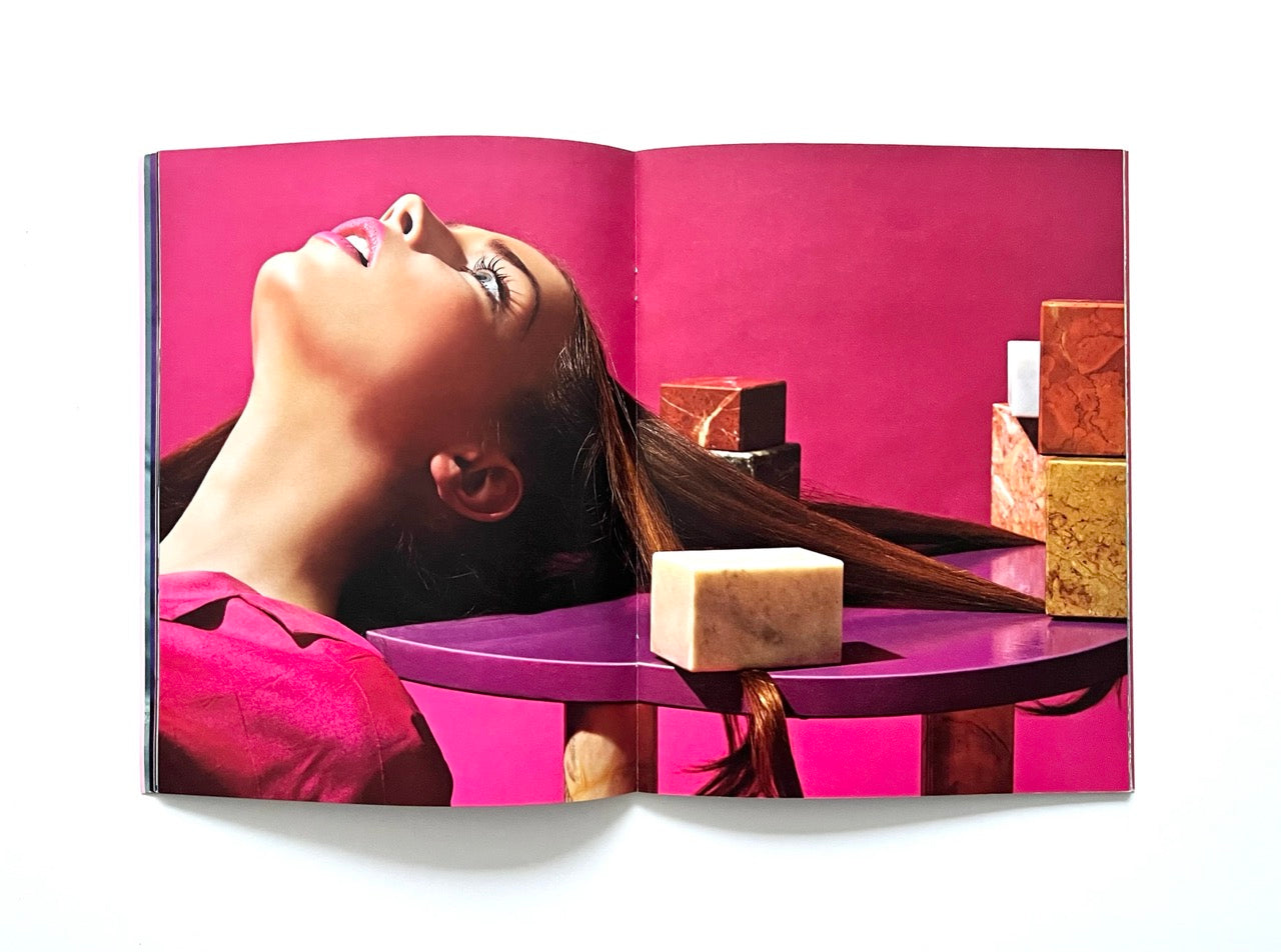 Magazine spread (Toiletpaper No. 7, December 2012) showing a woman's head  resting on a small round table, with strings of her hair stretched across it, held in place by blocks of marble.