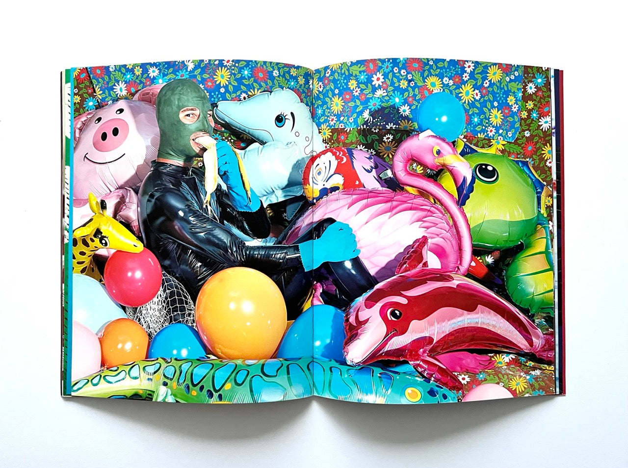 Magazine spread (Toiletpaper No. 7, December 2012) showing a man in a gimp mask, latex suit and rubber gloves sitting inside a pile of colourful inflateble animals.